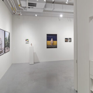 View of the exhibition space with artworks displayed on white walls and one sculpture displayed on a white plinth.
