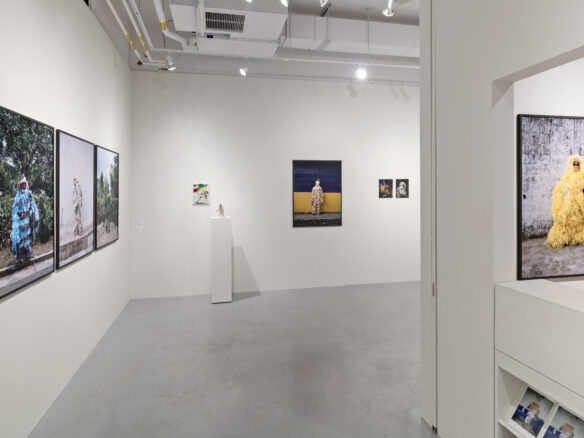View of the exhibition space with artworks displayed on white walls and one sculpture displayed on a white plinth.