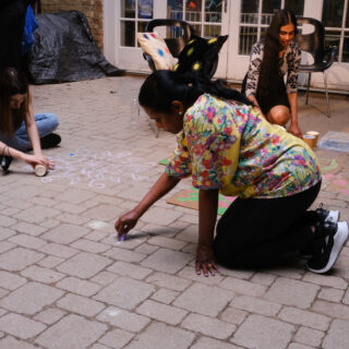 Individuals crouching and sitting closely together, focused on drawing kolam patterns on the brick floor.