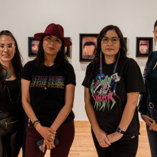 Four panelists from an artist talk stand side by side; a few smile while others have a neutral expression as they look toward the camera.