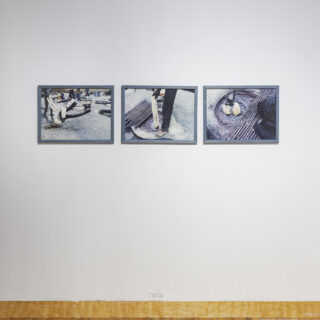 Three photographs in dyed blue frames hang on a white wall. The photographs depict traditional indigo dye bath processes in Ghana.