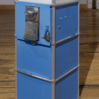 Close up of a blue candy machine with an embossed beaver on the coin slot cover.