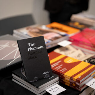 A table filled with multiple publications, in the foreground a black, softcover book is the focal point, titled "The Phantom" in serif white font.