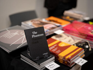 A table filled with multiple publications, in the foreground a black, softcover book is the focal point, titled "The Phantom" in serif white font.