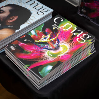 A brightly coloured issue of C Magazine with a pink and green plant on the cover sits on a black table-clothed table.