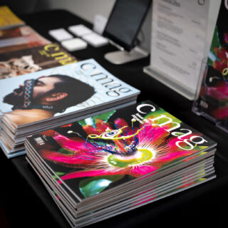 A black table-clothed table displays multiple issues of C Magazine.