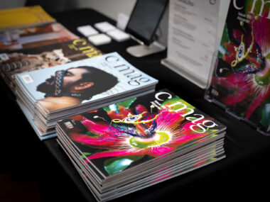 A black table-clothed table displays multiple issues of C Magazine.