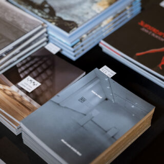 A black table-clothed table is stacked with multiple exhibition publications.