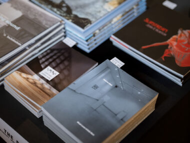 A black table-clothed table is stacked with multiple exhibition publications.