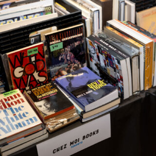 A sign reading "Chez Moi Books" hangs off a table stacked full of various vintage books.