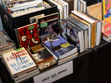 A sign reading "Chez Moi Books" hangs off a table stacked full of various vintage books.