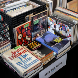 A table with a black milk crate is staked with many books.