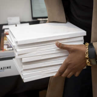 A black skinned person holds a stack of white, hard covered books.