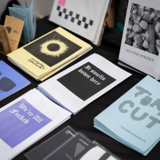 A table with a black tablecloth displays multiple zines, including titled "Torn Cut", "We're All Fucked", and "Poutine Politics".