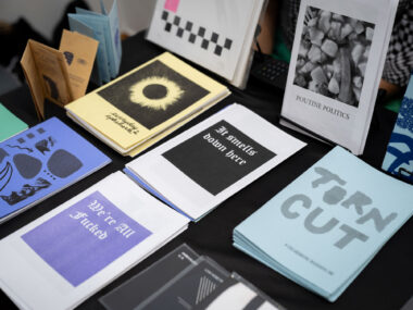 A table with a black tablecloth displays multiple zines, including titled "Torn Cut", "We're All Fucked", and "Poutine Politics".