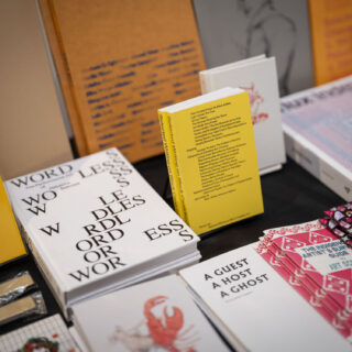 A table is stacked with multiple books, zines, and publications.