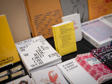 A black table-clothed table filled with books features titles including "WORDLESS", "A Guest A Host A Ghost", and "Selected Writings on Black Canadian Art".