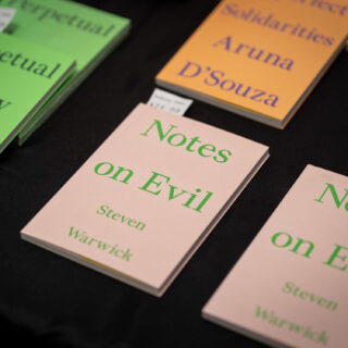 Close up of a table highlighting the a book with a pale pink cover titled "Notes on Evil" in green text.