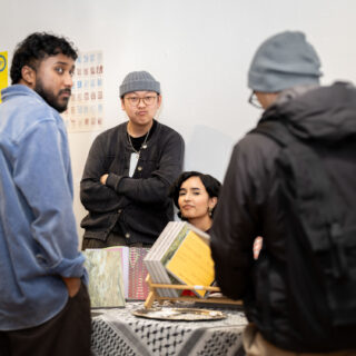 Four young people of varying skin tones crowd around a table draped with a kuffiyeh, displaying copies of PATINAPATINA Magazine.