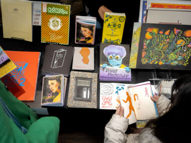 Various colourful, risograph printed zines and prints are displayed on a table with a black table cloth.