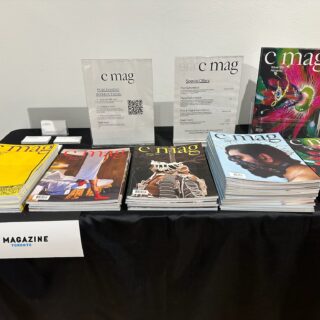 A white sign reading "C Magazine" hangs from a black table-clothed table displaying multiple magazine issues and special offer flyers.