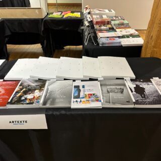 A sign reading "Artexte" hangs from a black table-clothed table with various art books on display.