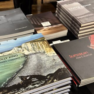 A black table-clothed table is stacked with multiple exhibition publications.