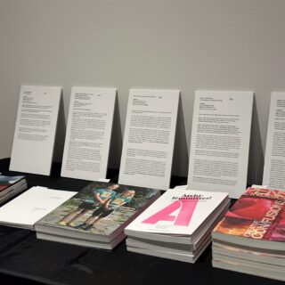 A table with a black tablecloth is stacked with five different books. White print outs provide information on each publication in French and English.