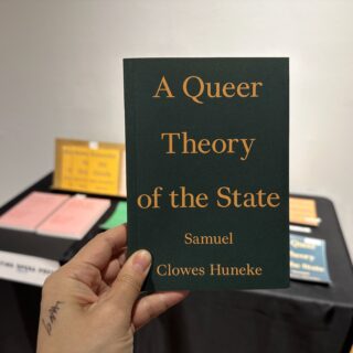 A light skinned hand holds a dark green book titled "A Queer Theory of the State" in orange serif font.