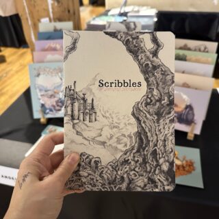 A light skinned hand holds a book titled "Scribbles: An Annotated Sketchbook".