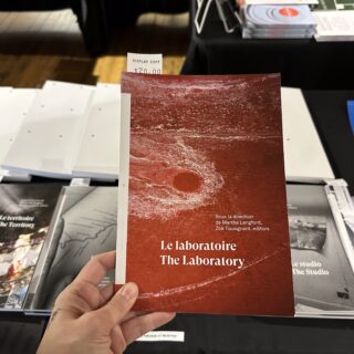 A light skinned hand holds a red book titled "La Laboratorie".