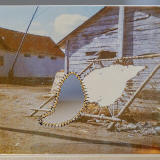 A vintage photo of a building with a weathered wooden wall. There is a gold-stitched cutout in the centre of the image, whose loose oval shape reveals an abstract blurry background behind the photo.