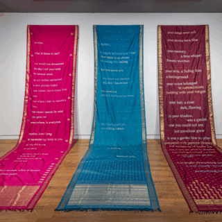 Installation view of pink, blue, and maroon sarees with golden texts and decorations.