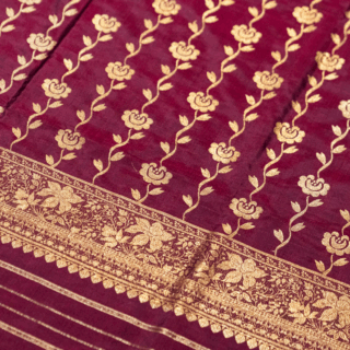 A close-up for maroon saree adorned with intricate golden floral patterns and a decorative border.