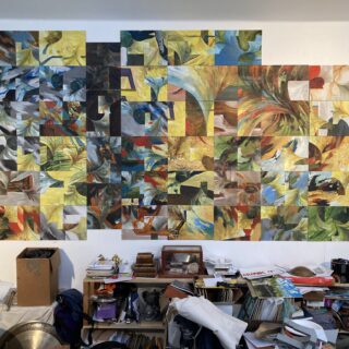 A large assemblage of colourful abstract paintings takes up an entire wall in an artist's cluttered studio