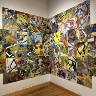 Corner wall covered with a grid of colourful abstract paintings forming one large installation.