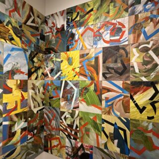 Corner of a white wall covered in colourful abstract paintings arranged in a grid