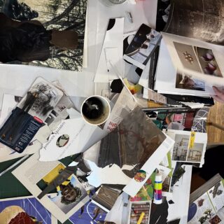 Table covered with assorted collage materials, including paper scraps, magazines, pastels, pencils, and three cups.