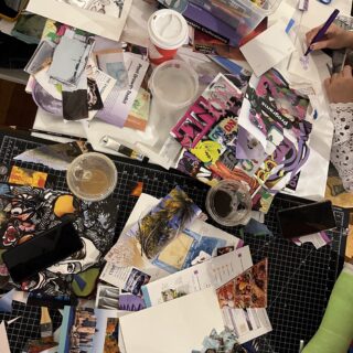 Table covered with assorted collage materials, including paper scraps, scissors, magazine clippings, and a bin full of markers, pencils, and pens.
