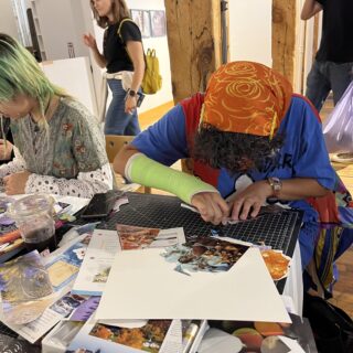 Two people sitting at a table, making paper collages, with their hands actively at work.