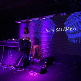 A DJ performs at a turntable in front of a brick wall with "Hiba Salameh" projected behind them.